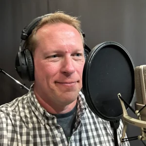 C.L. Berns recording voice-over in a studio while wearing headphones and speaking into a microphone with a pop filter